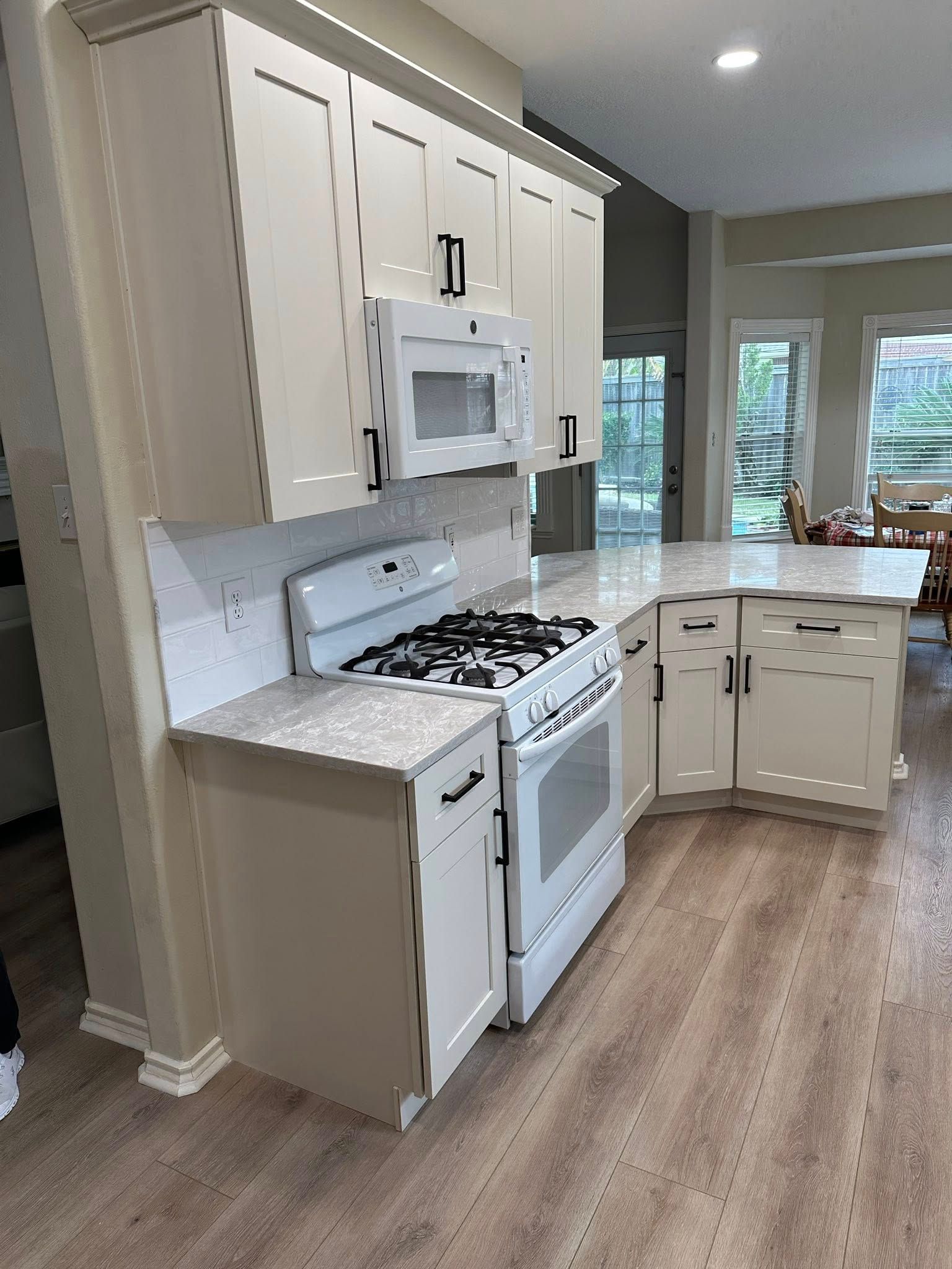 Bright kitchen with white cabinets, white appliances, gray countertops, and wood-look flooring.
