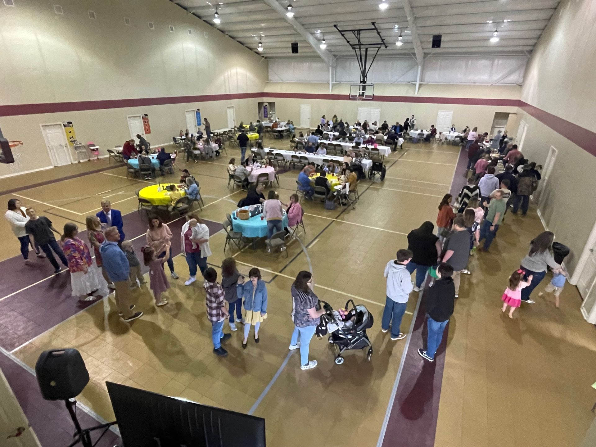A large group of people are standing around tables in a gym.