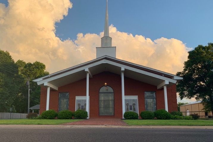 A church with a steeple is sitting on the side of the road.