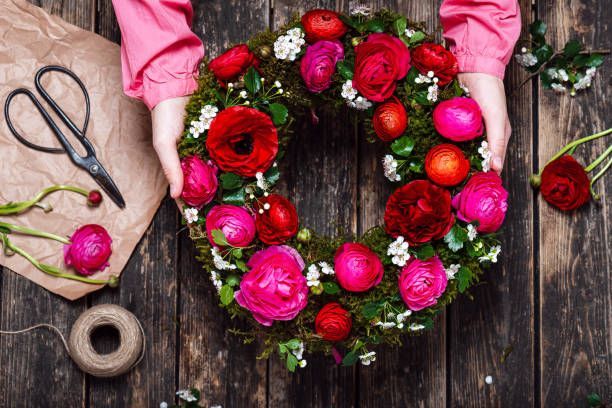A person is holding a wreath of flowers on a wooden table.