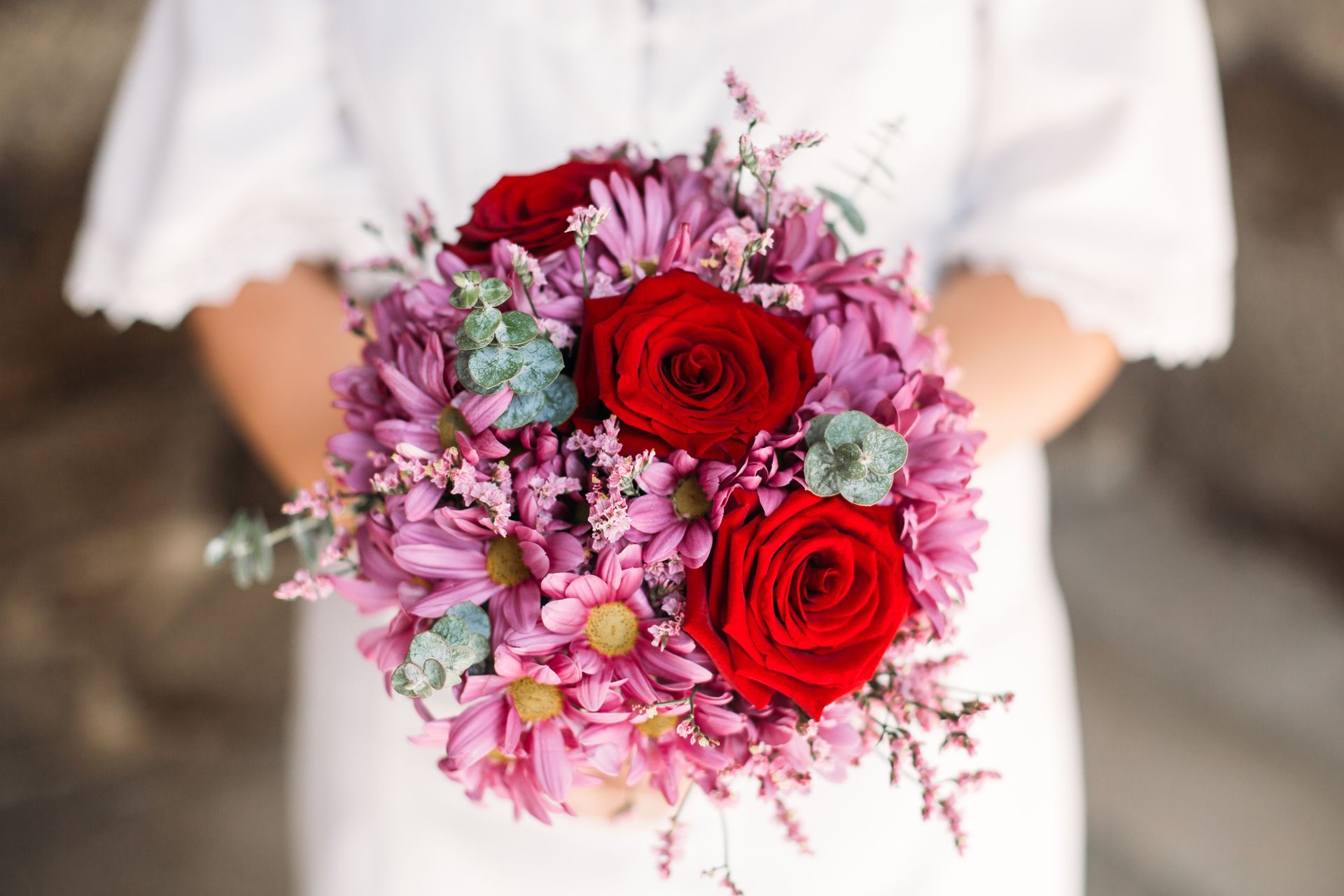 A woman is holding a bouquet of pink and red flowers.
