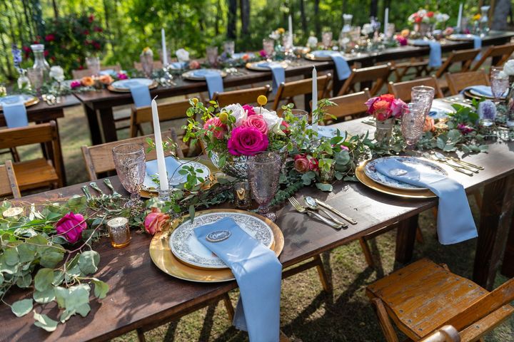 A long table is set for a wedding reception with plates , napkins , candles and flowers.