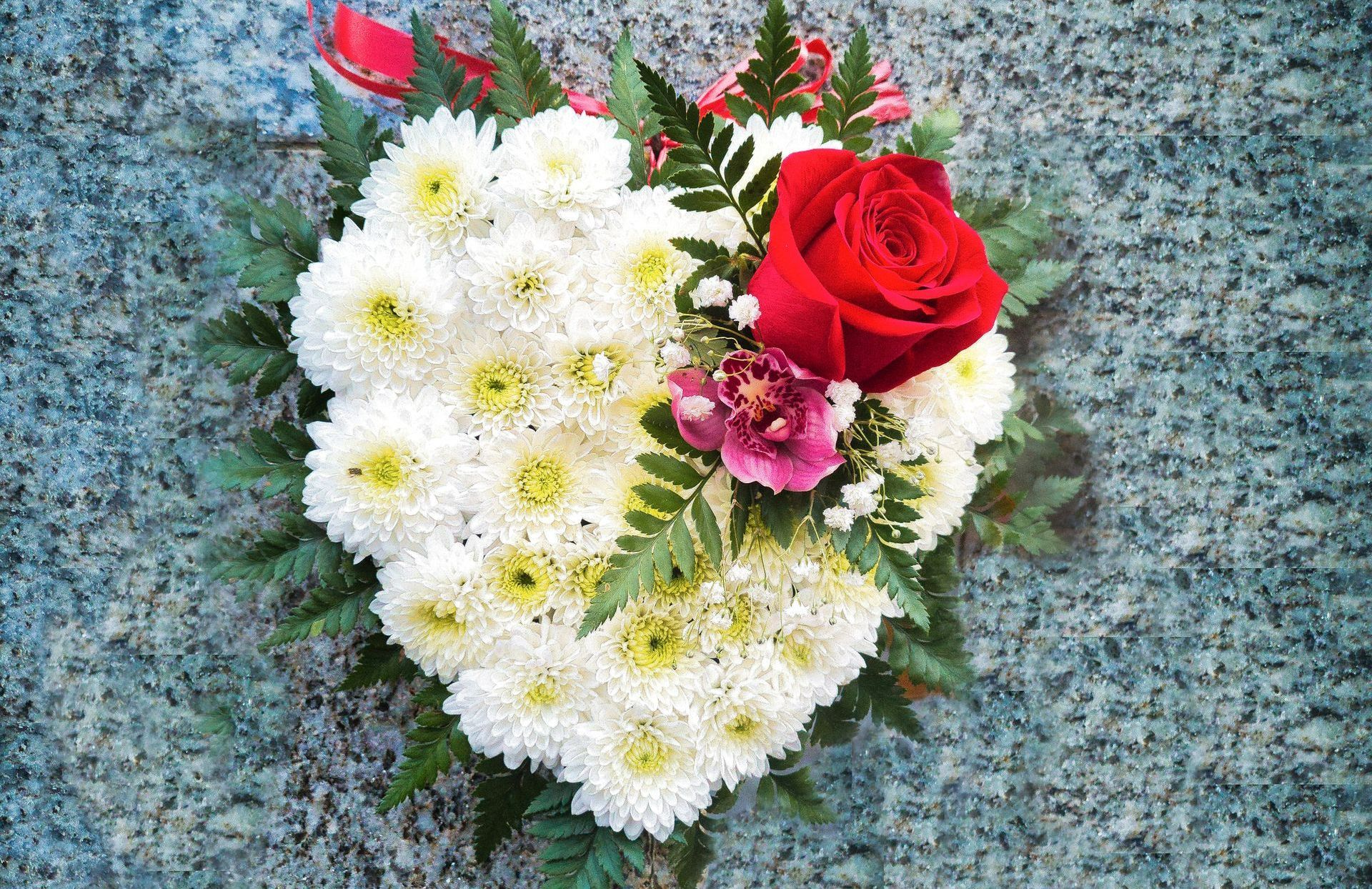 A heart shaped bouquet of flowers with a red rose in the middle.