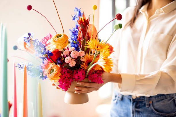 A woman is holding a vase filled with colorful flowers.