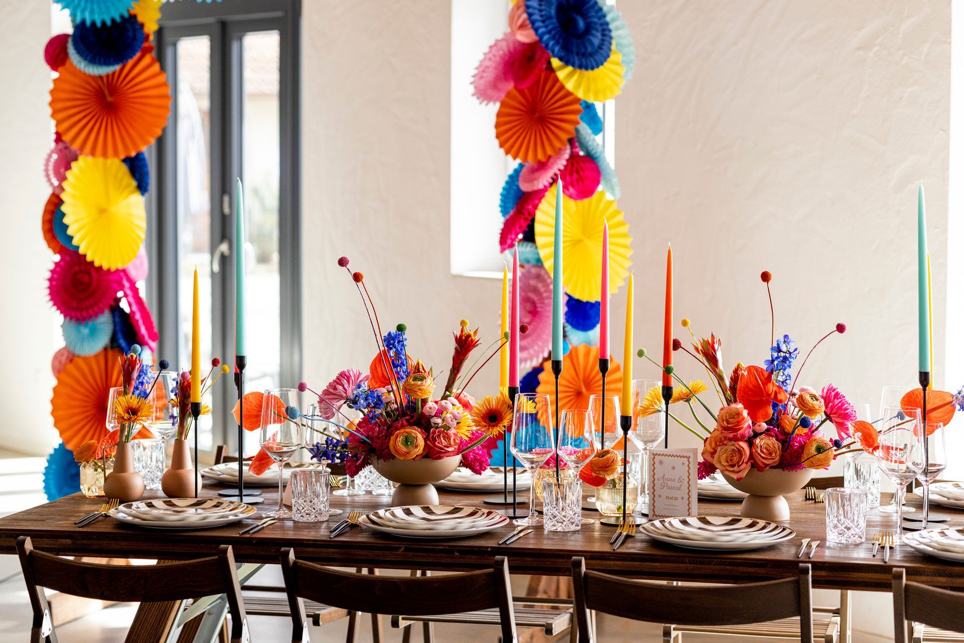 A dining room table decorated with colorful paper fans and candles. A dining room table decorated with colorful paper fans and candles.