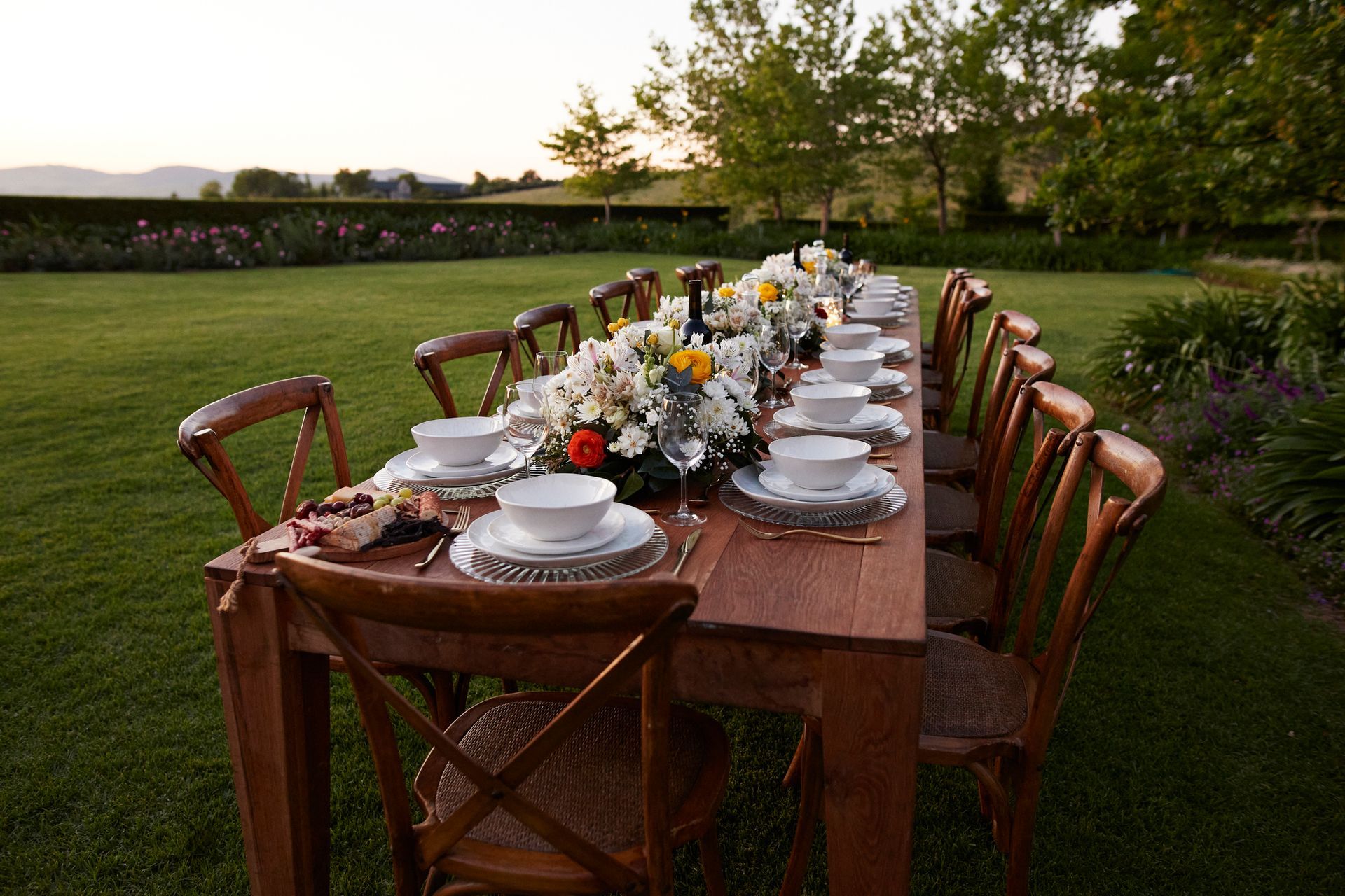 A long wooden table with plates and bowls on it is sitting on top of a lush green field.