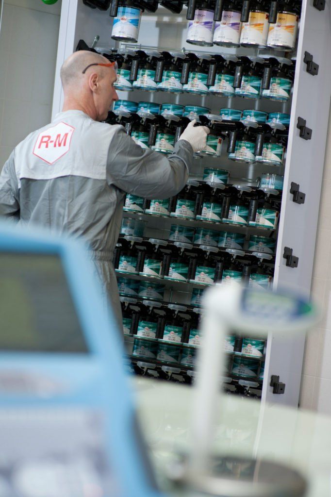 A man is standing in front of a shelf filled with bottles of paint.