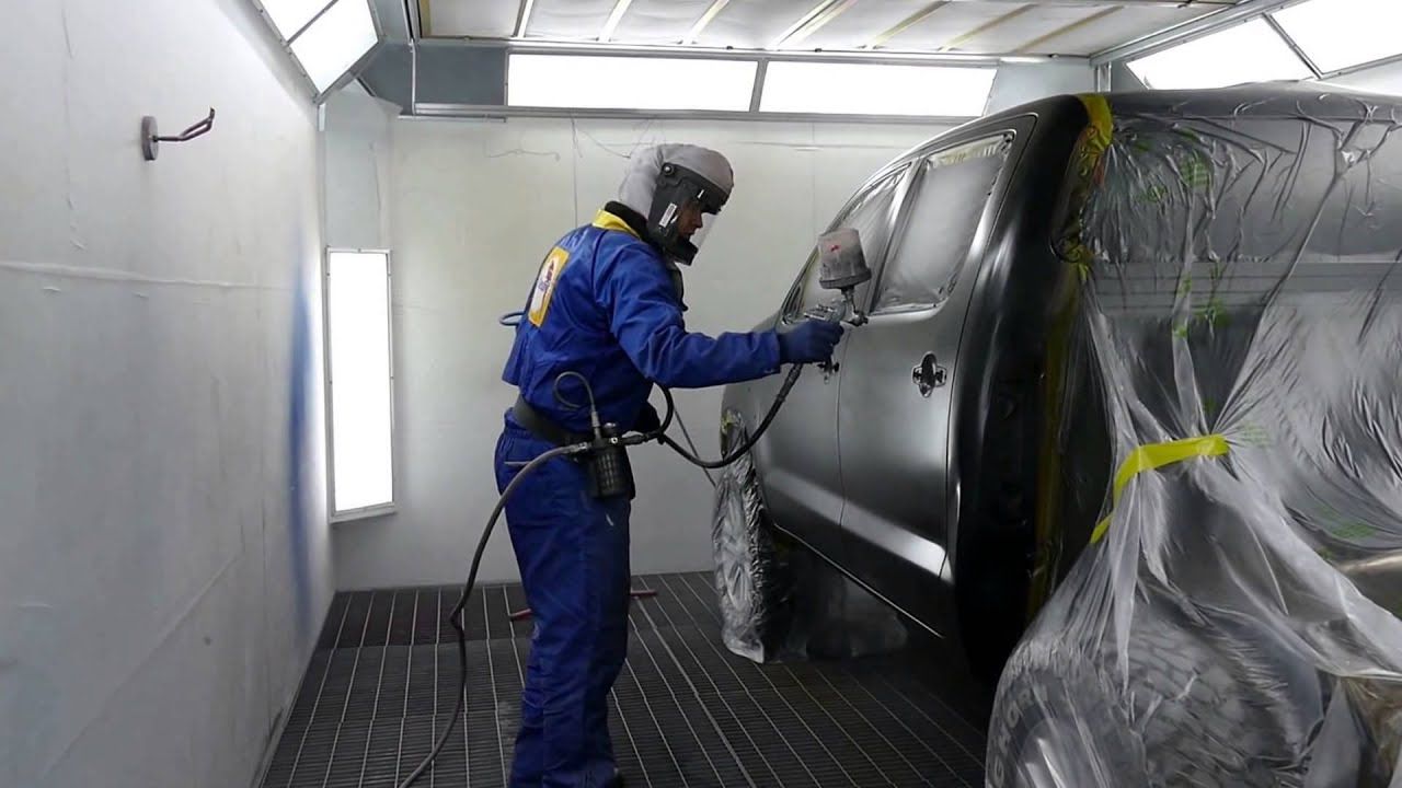 A man is painting a car in a paint booth.