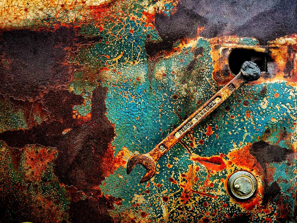 A rusty wrench is laying on a rusty surface.
