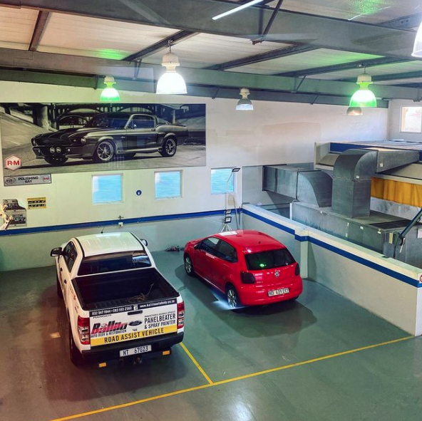 A red car is parked next to a white truck that says mercedes benz