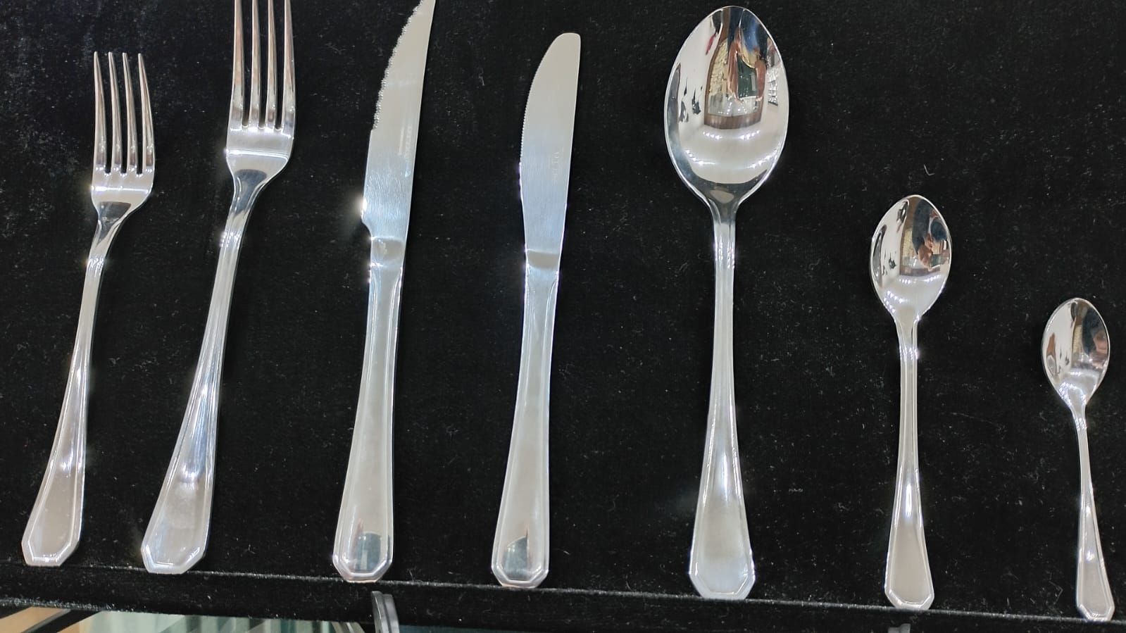Una fila de cubiertos que incluyen cuchillos, tenedores y cucharas sobre una superficie negra