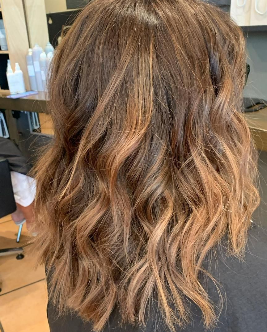 A Woman With Long Wavy Brown Hair is Sitting in a Chair in a Salon — Energy Hair Co in Noosa Heads, QLD