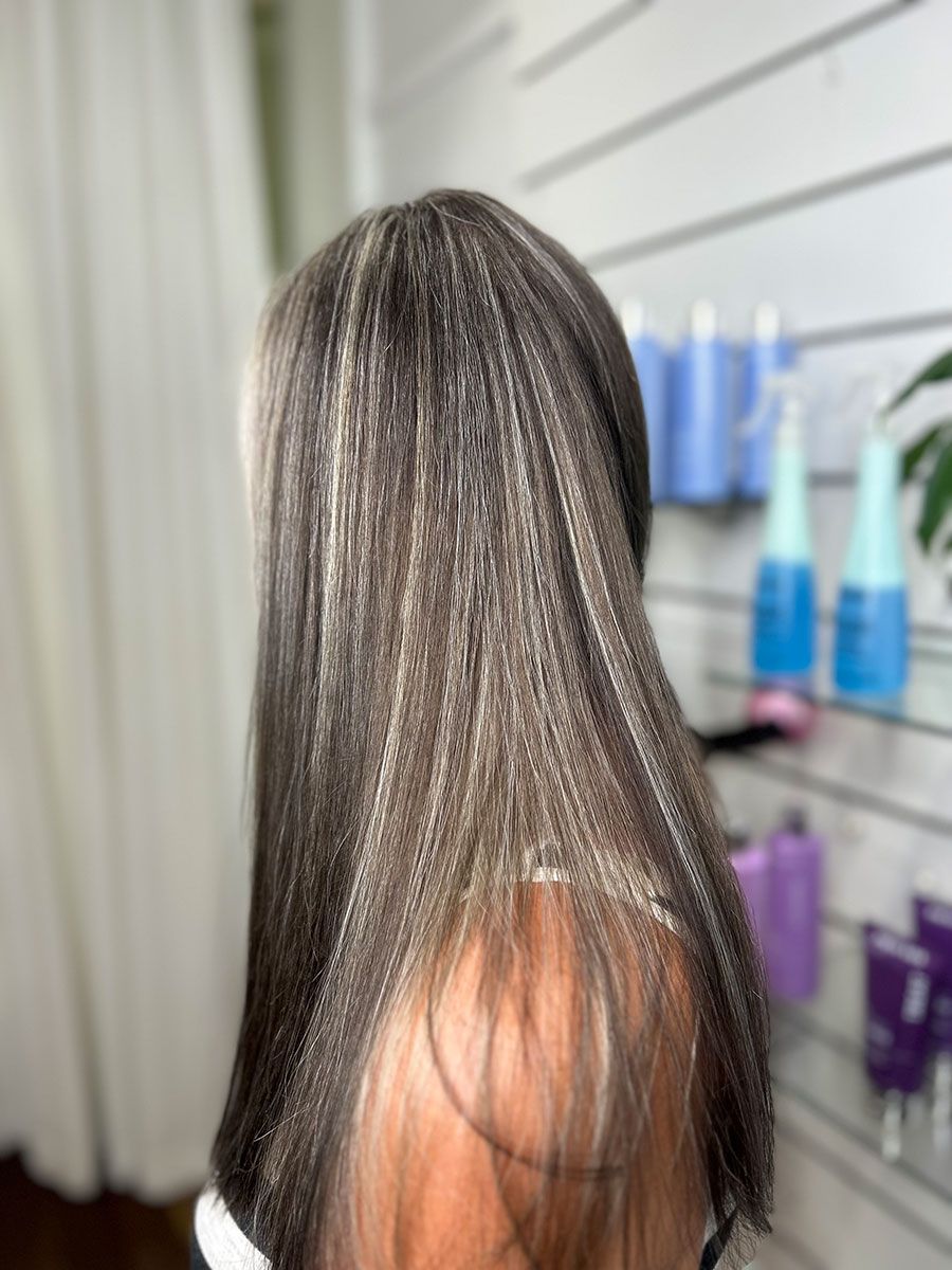 A Woman With Long Hair is Standing in Front of a Wall With Bottles of Hair Products — Energy Hair Co in Noosa Heads, QLD
