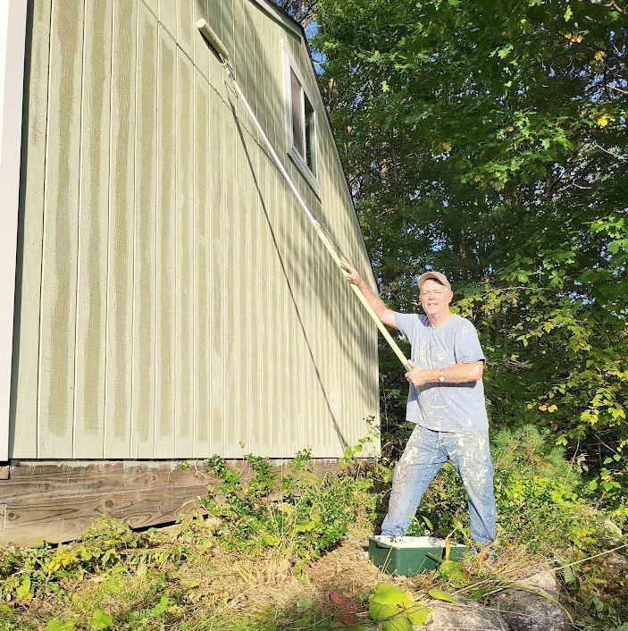 A man is painting the side of a house with a roller paint
