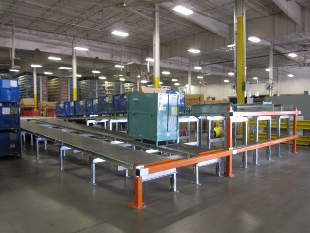 Factory floor with a conveyor belt system and machinery, including a green cabinet, under bright lights.