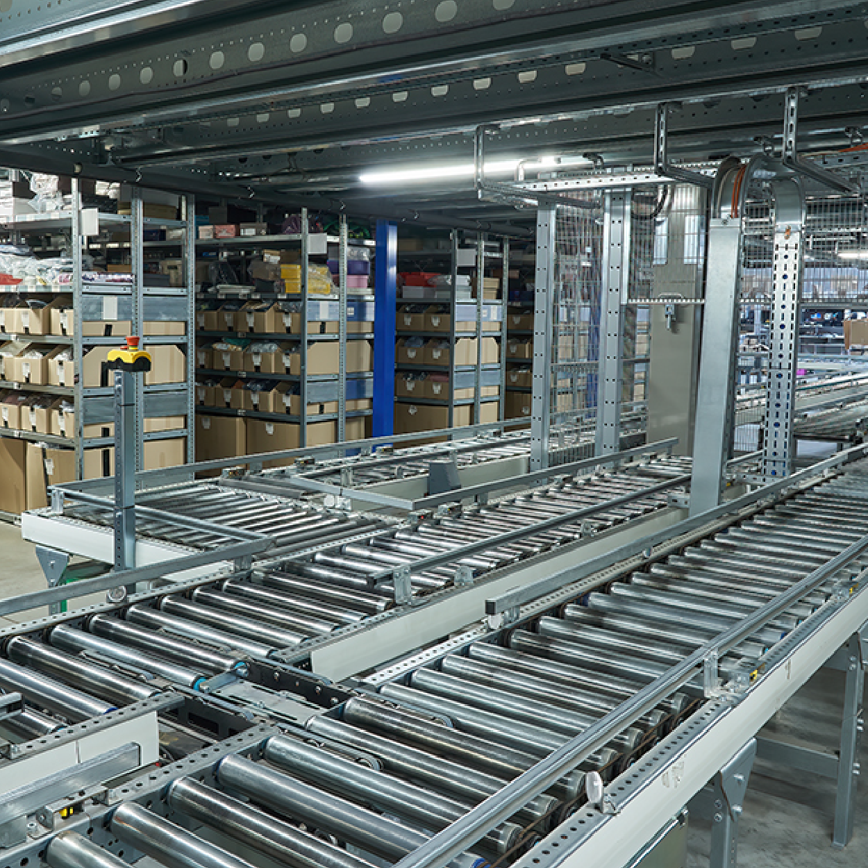 Automated warehouse conveyor system with metal rollers and shelving stocked with boxes