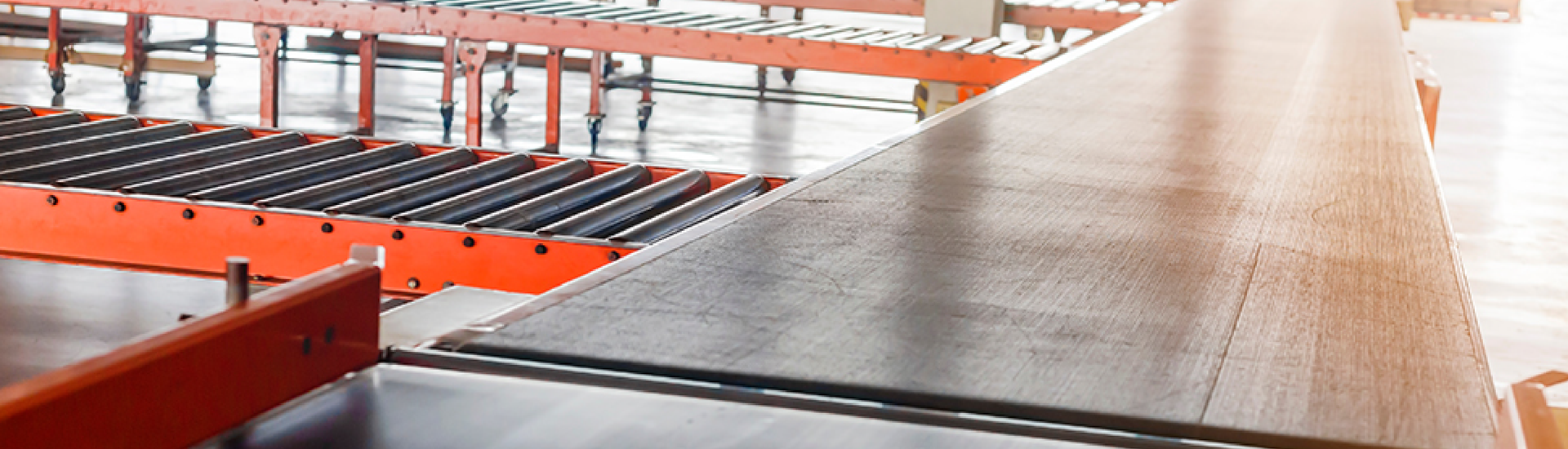 Modern industrial conveyor belt with orange rollers and a wooden platform in a factory setting