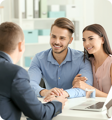 A couple smiles while meeting with a real estate agent at a desk.