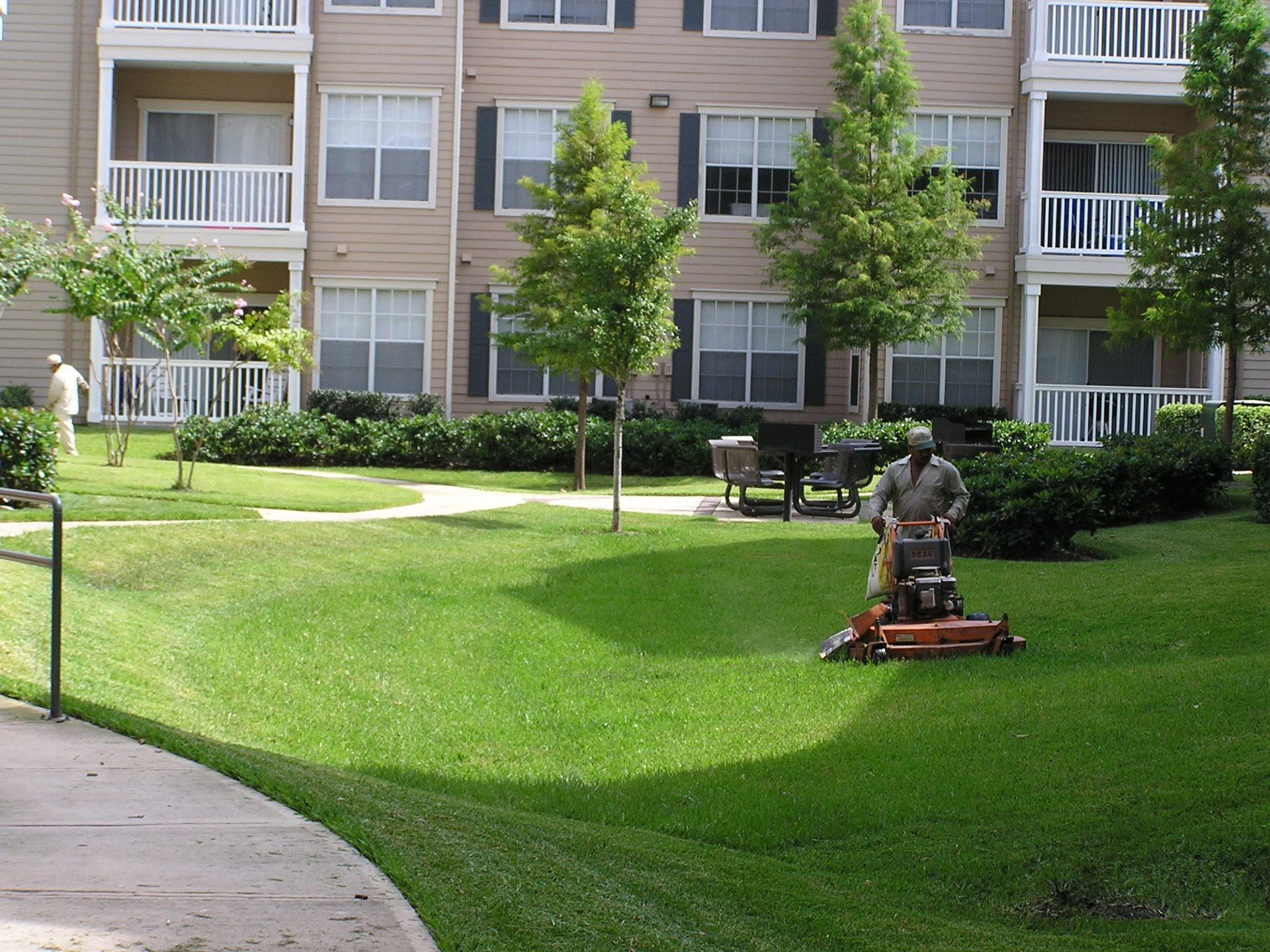 A man is mowing a lush green lawn in front of a building