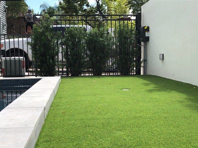 A lawn with a fence and a pool in the background