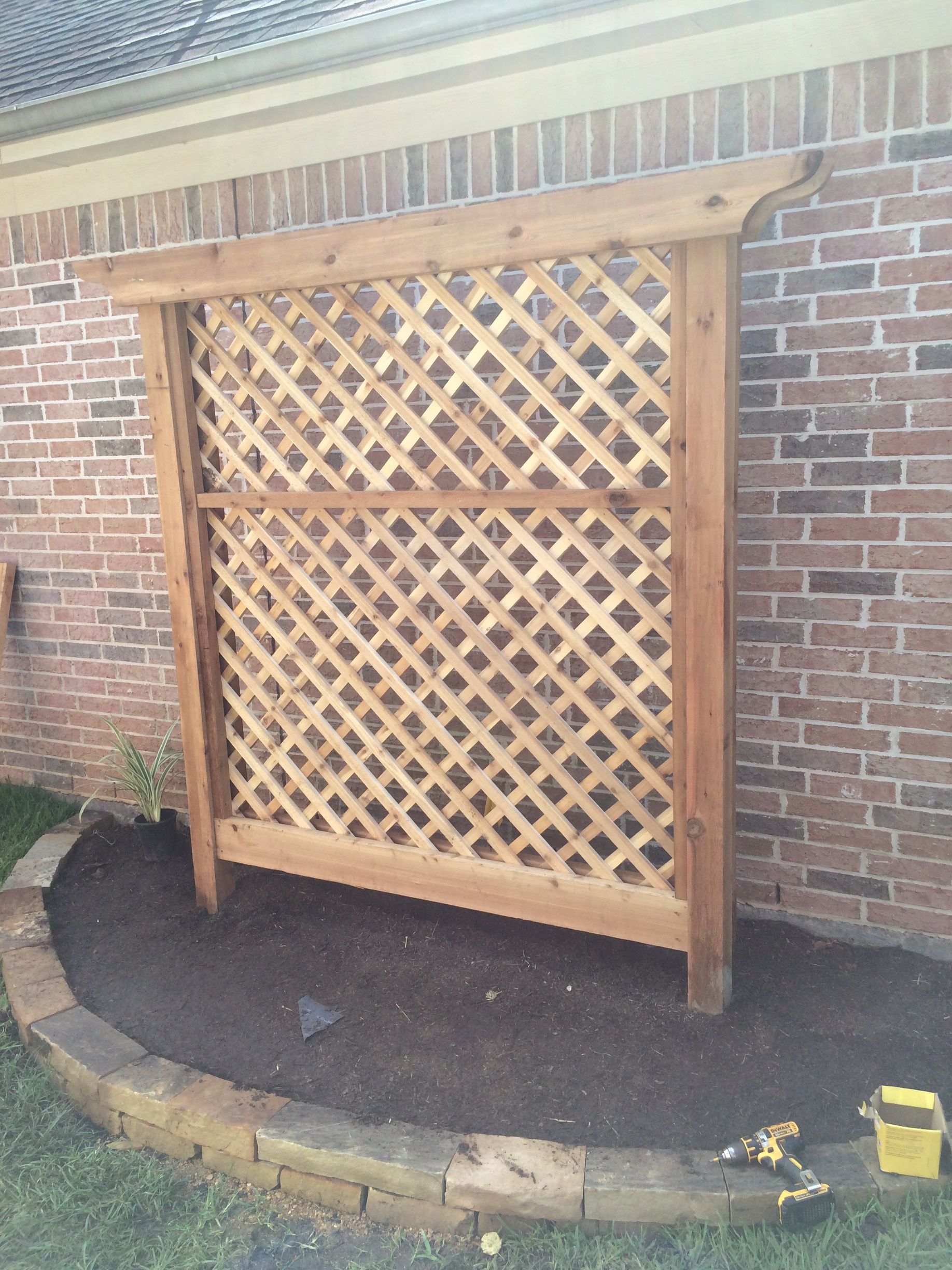A wooden trellis is sitting in front of a brick wall.