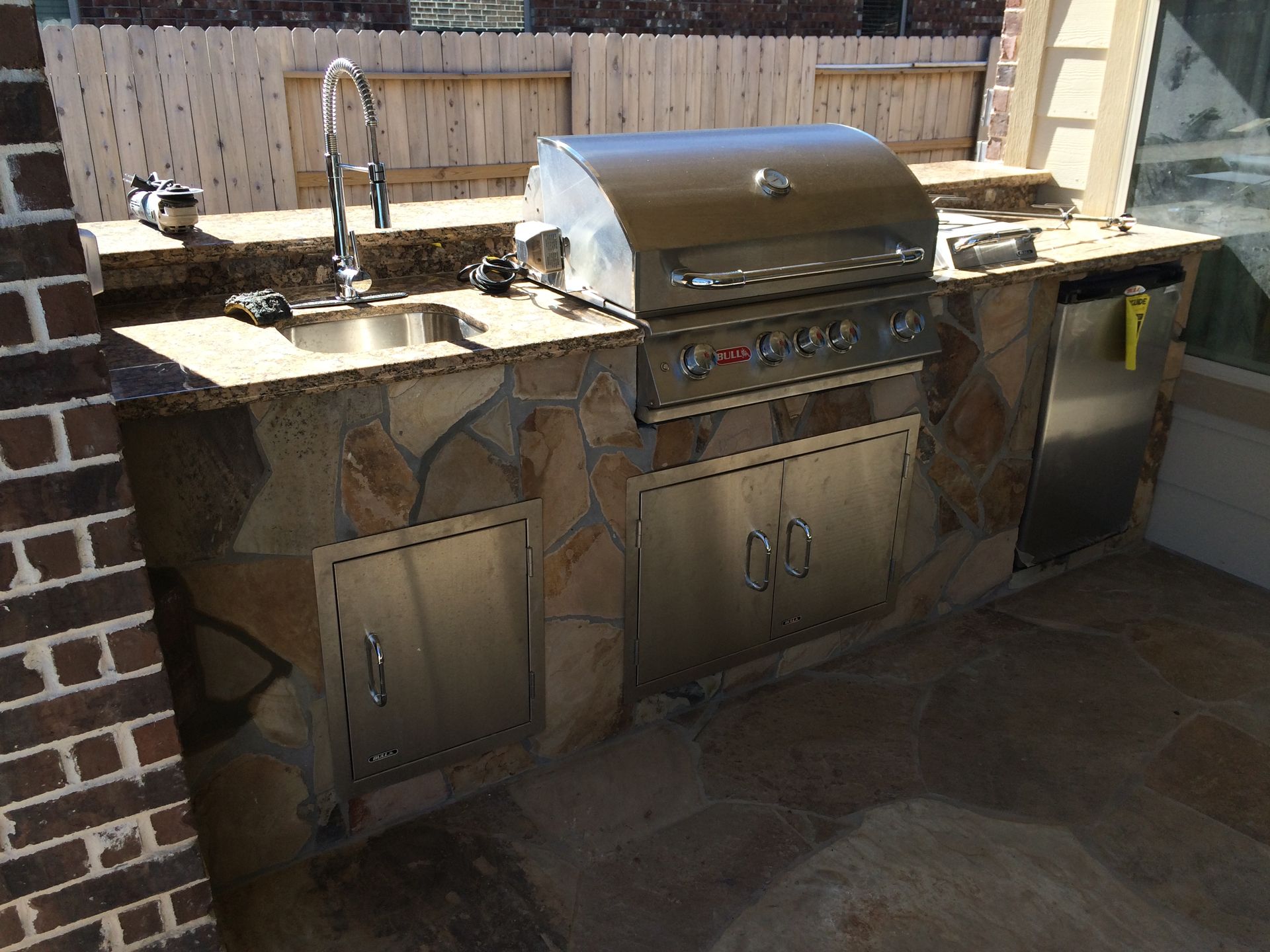 An outdoor kitchen with a stainless steel grill and a sink