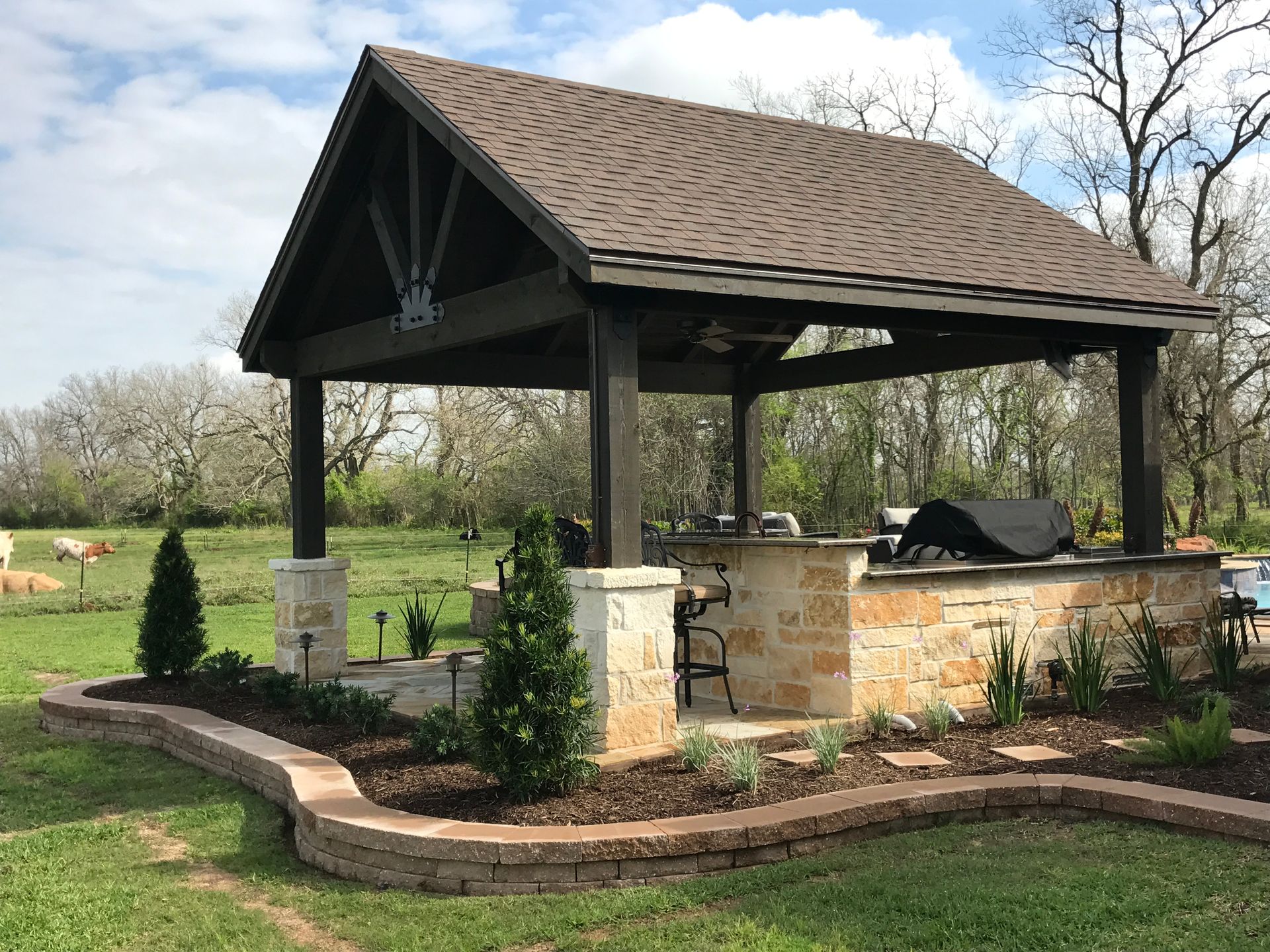 There is a gazebo with a grill inside of it in the middle of a field.