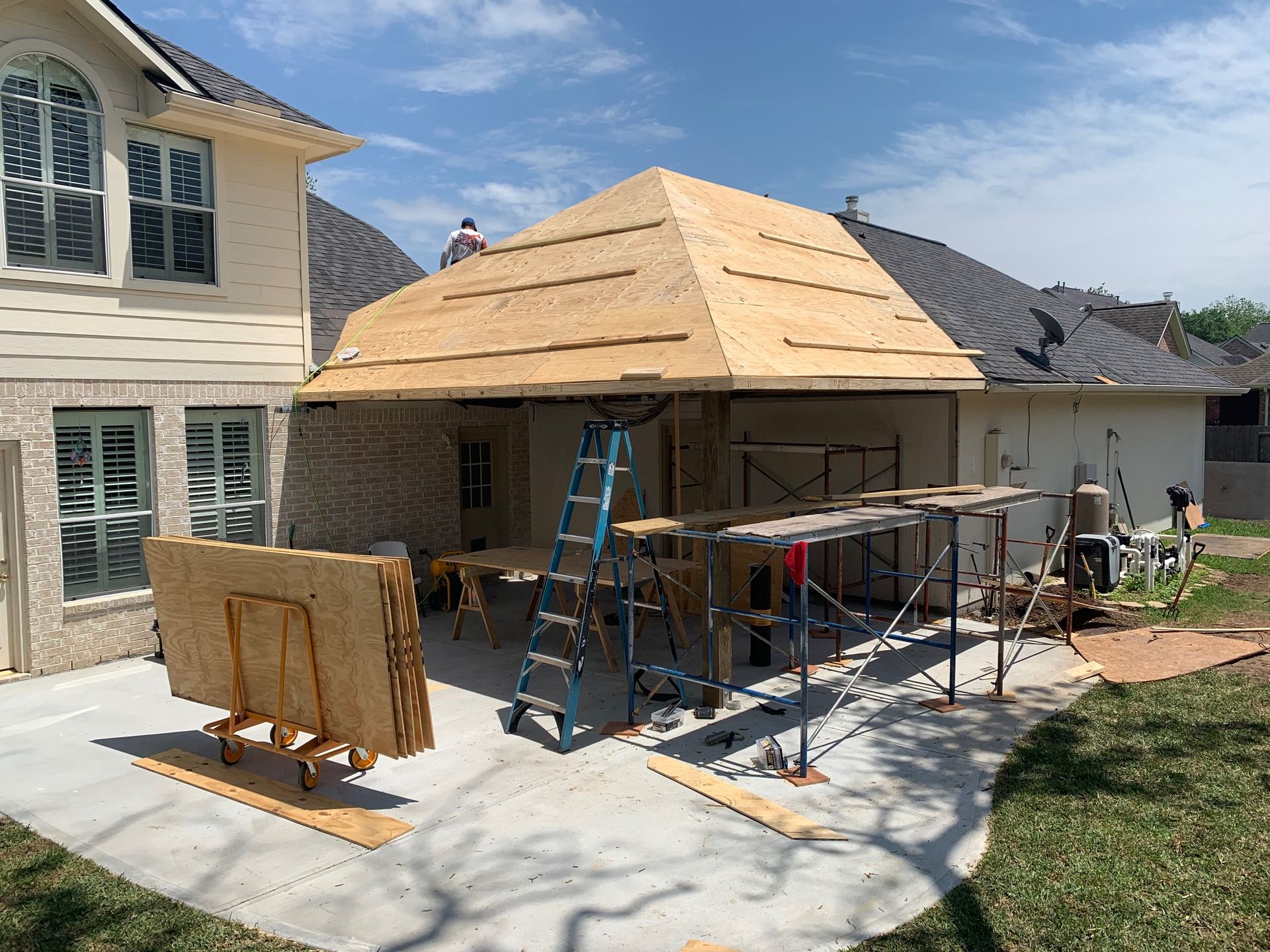 A man is standing on top of a wooden structure in front of a house.