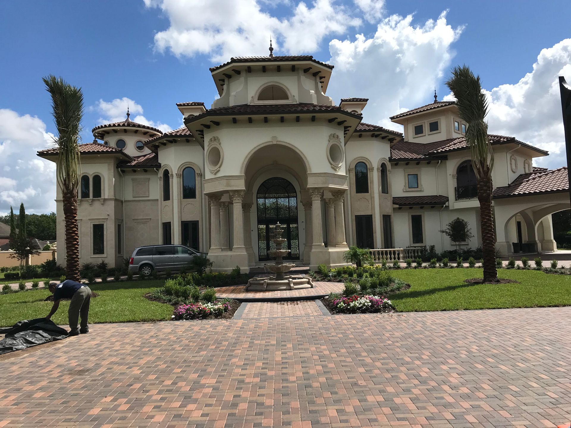 A large white house with a brick driveway and palm trees in front of it.
