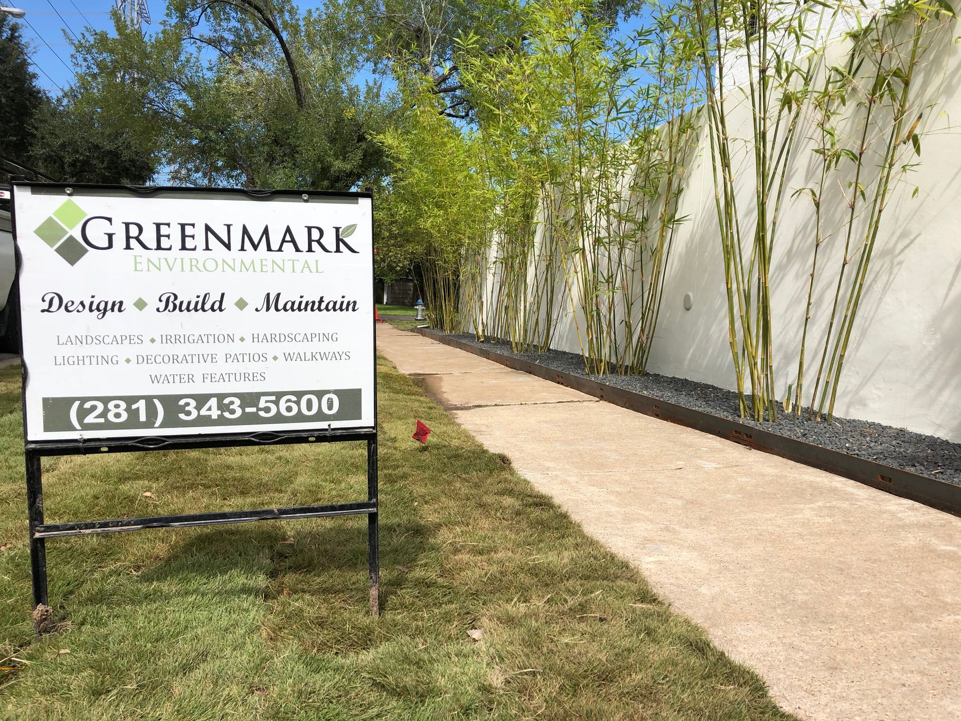 A sign for greenmark is sitting in the grass next to a sidewalk.
