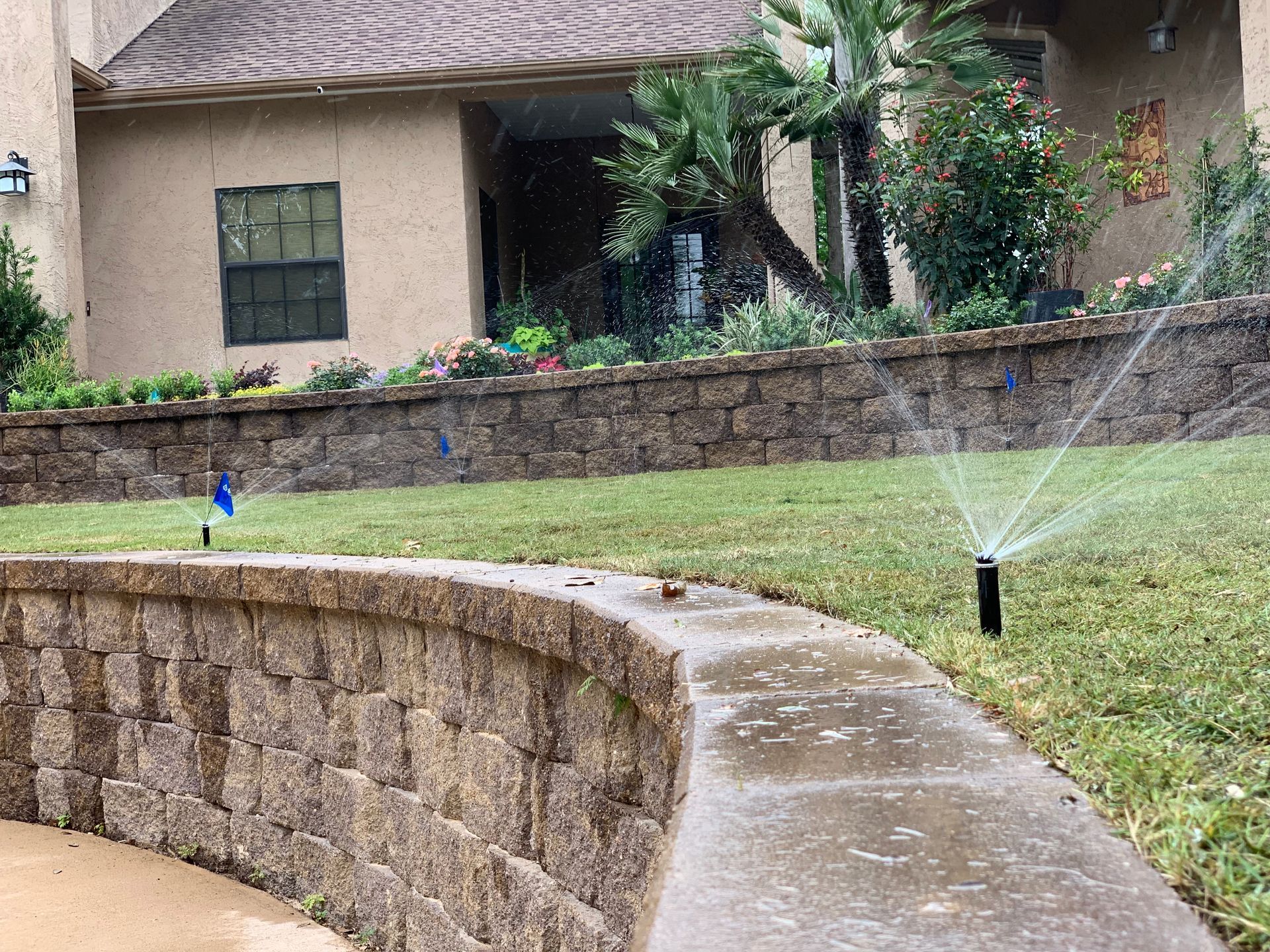 A lawn sprinkler is spraying water on a lush green lawn in front of a house.