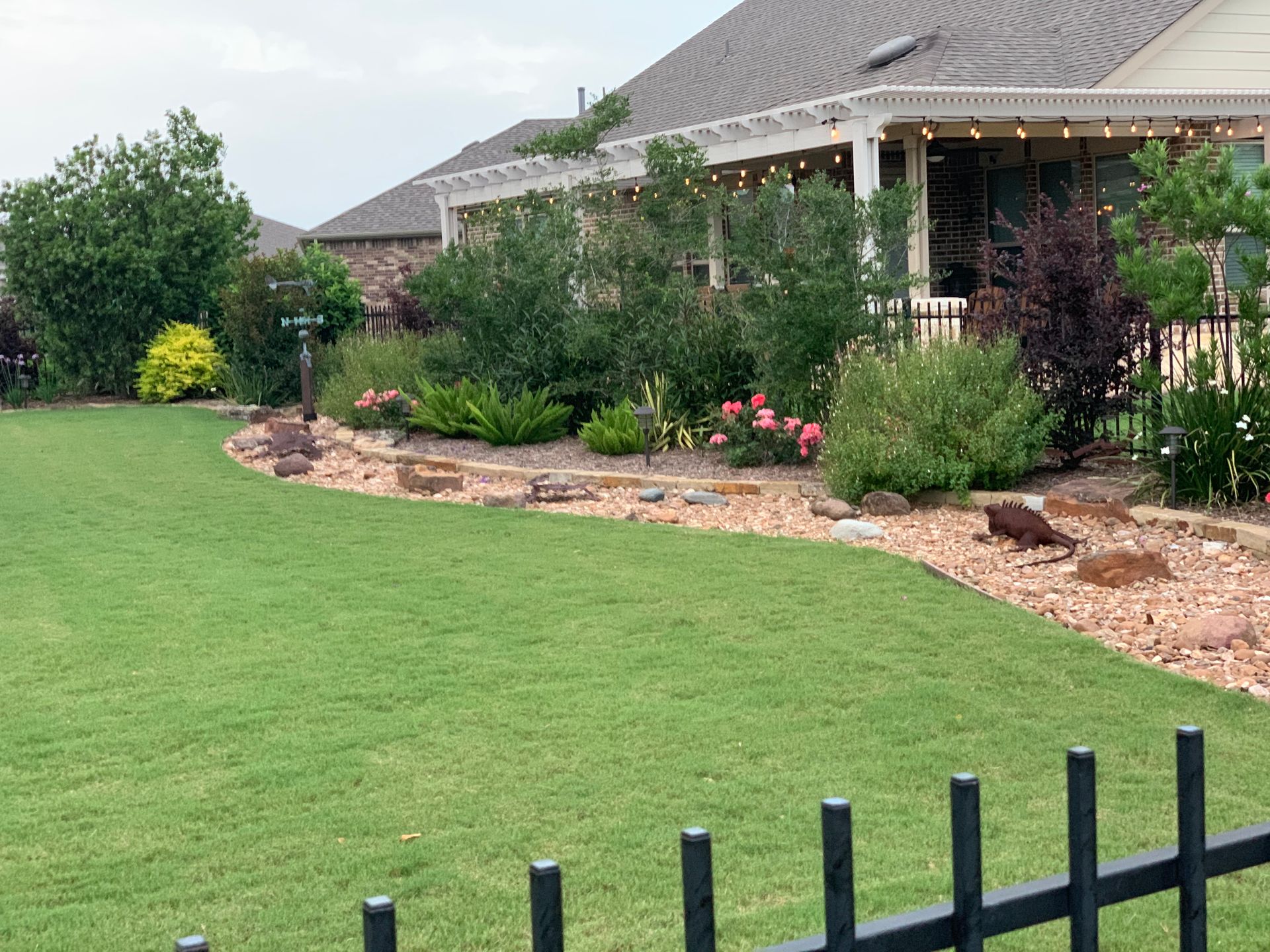 A fence surrounds a lush green lawn in front of a house