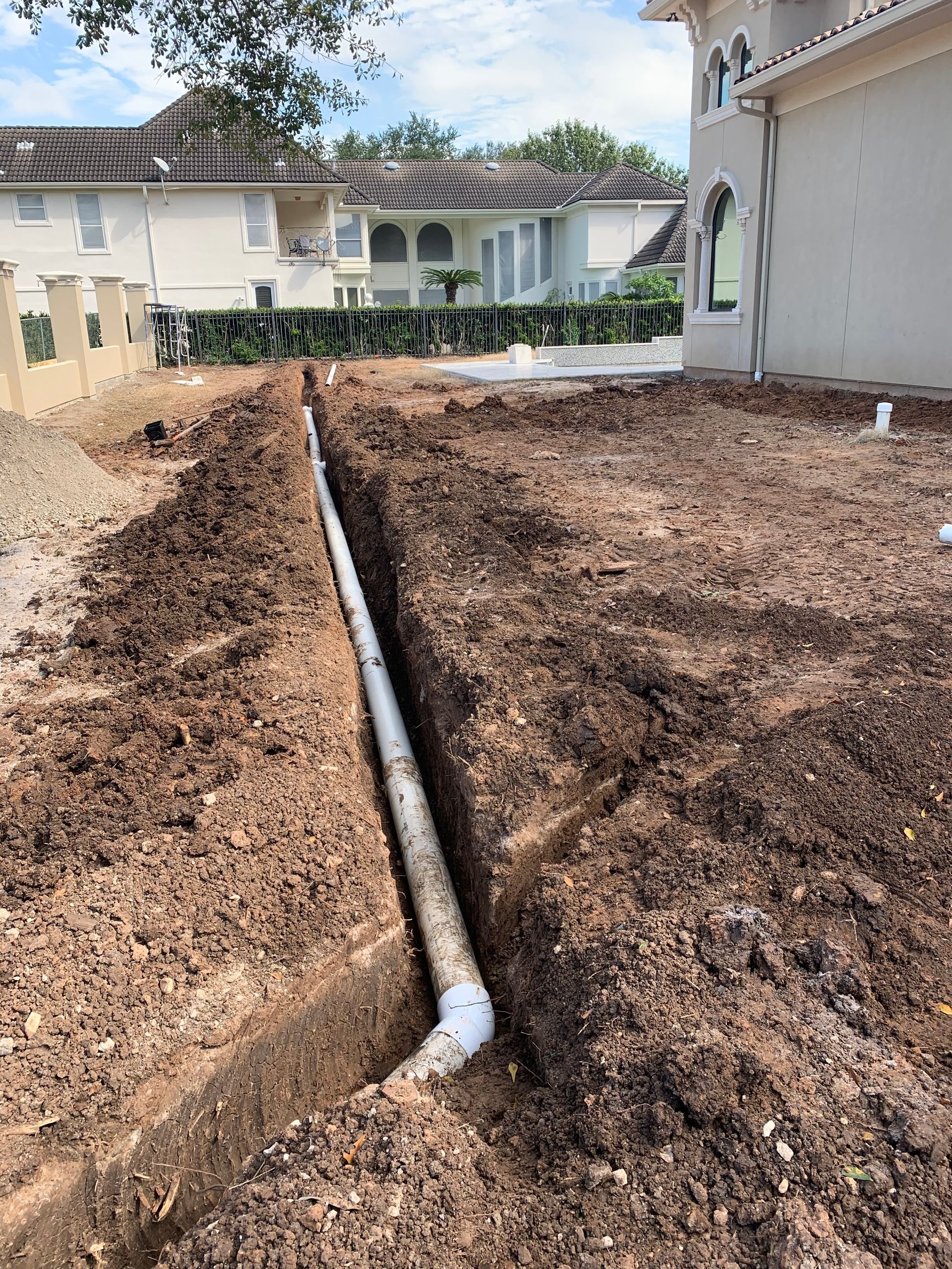 A drain pipe is being installed in the dirt in front of a house.