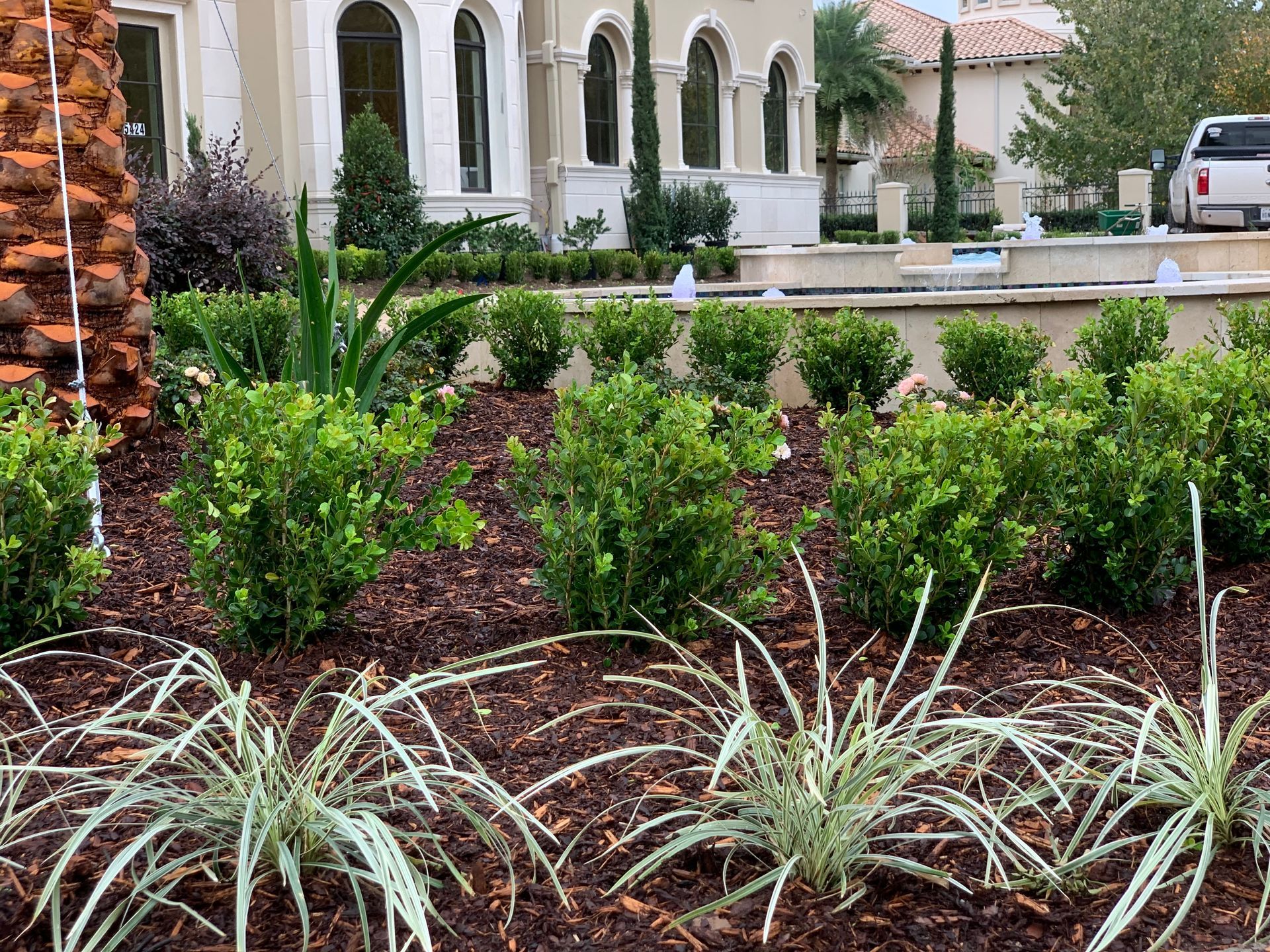 A lush green garden in front of a house with a fountain in the background.