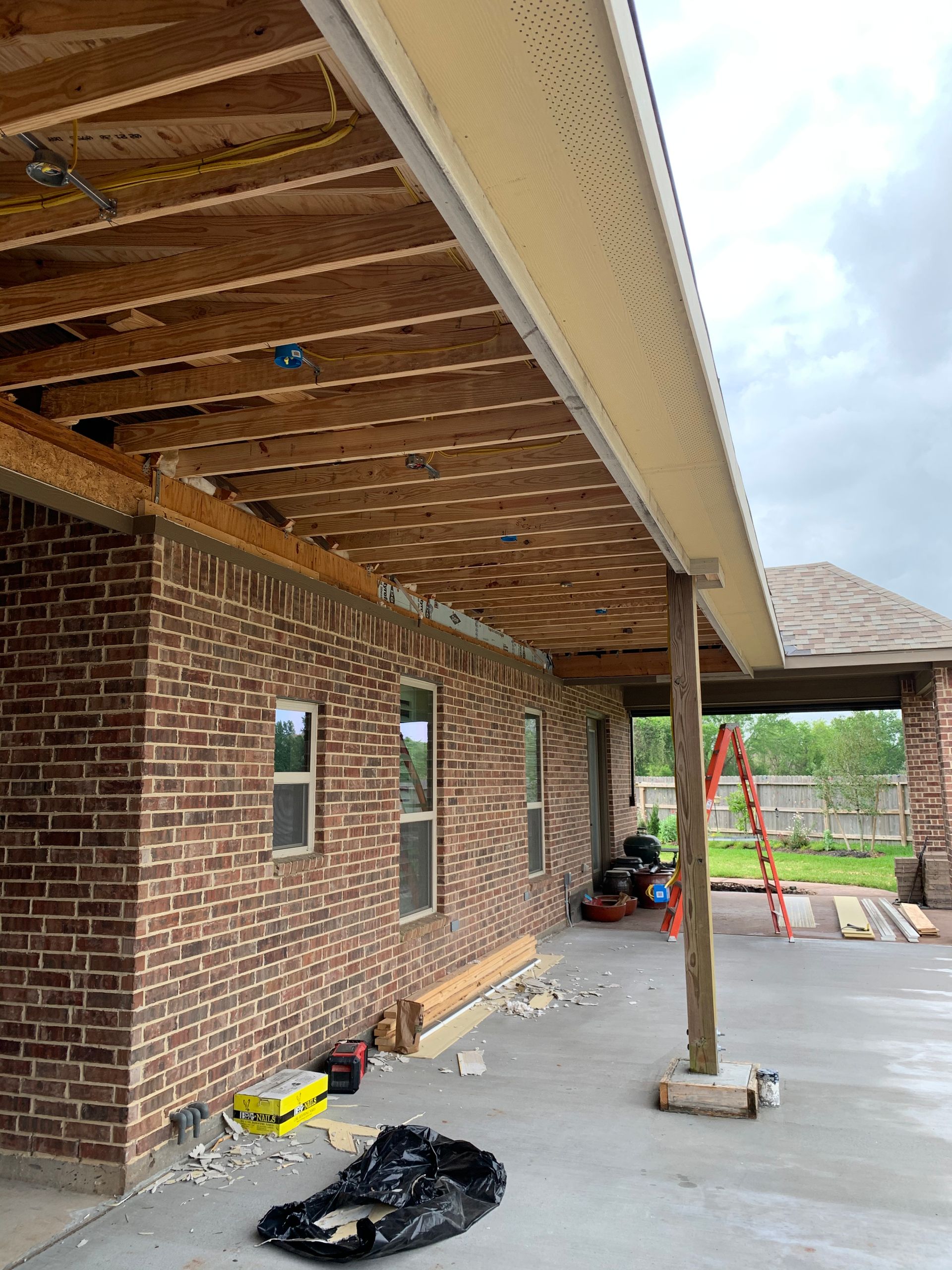 A brick house under construction with a wooden roof and a ladder.