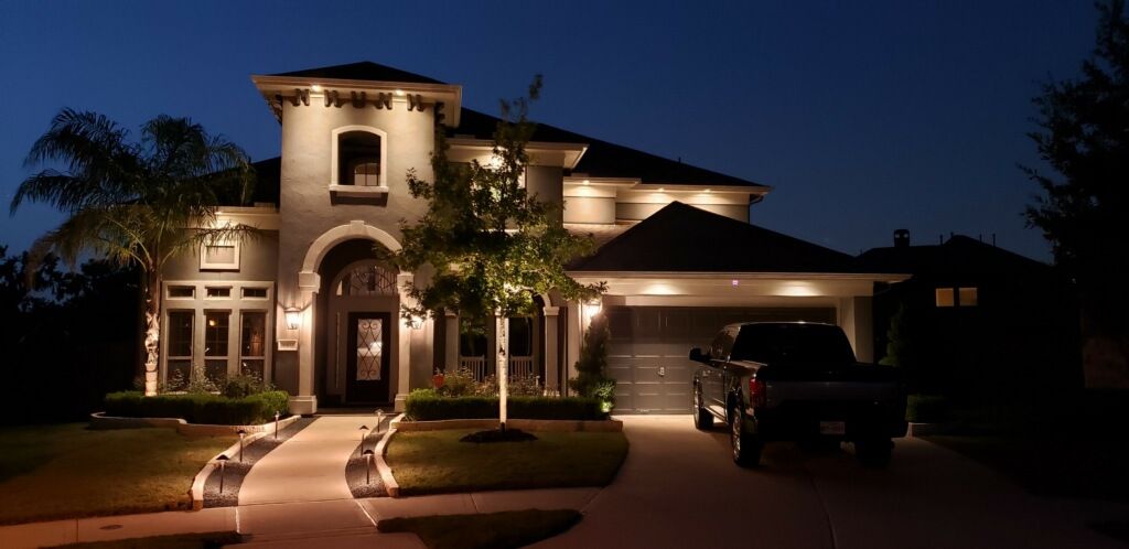 A large house is lit up at night with cars parked in front of it