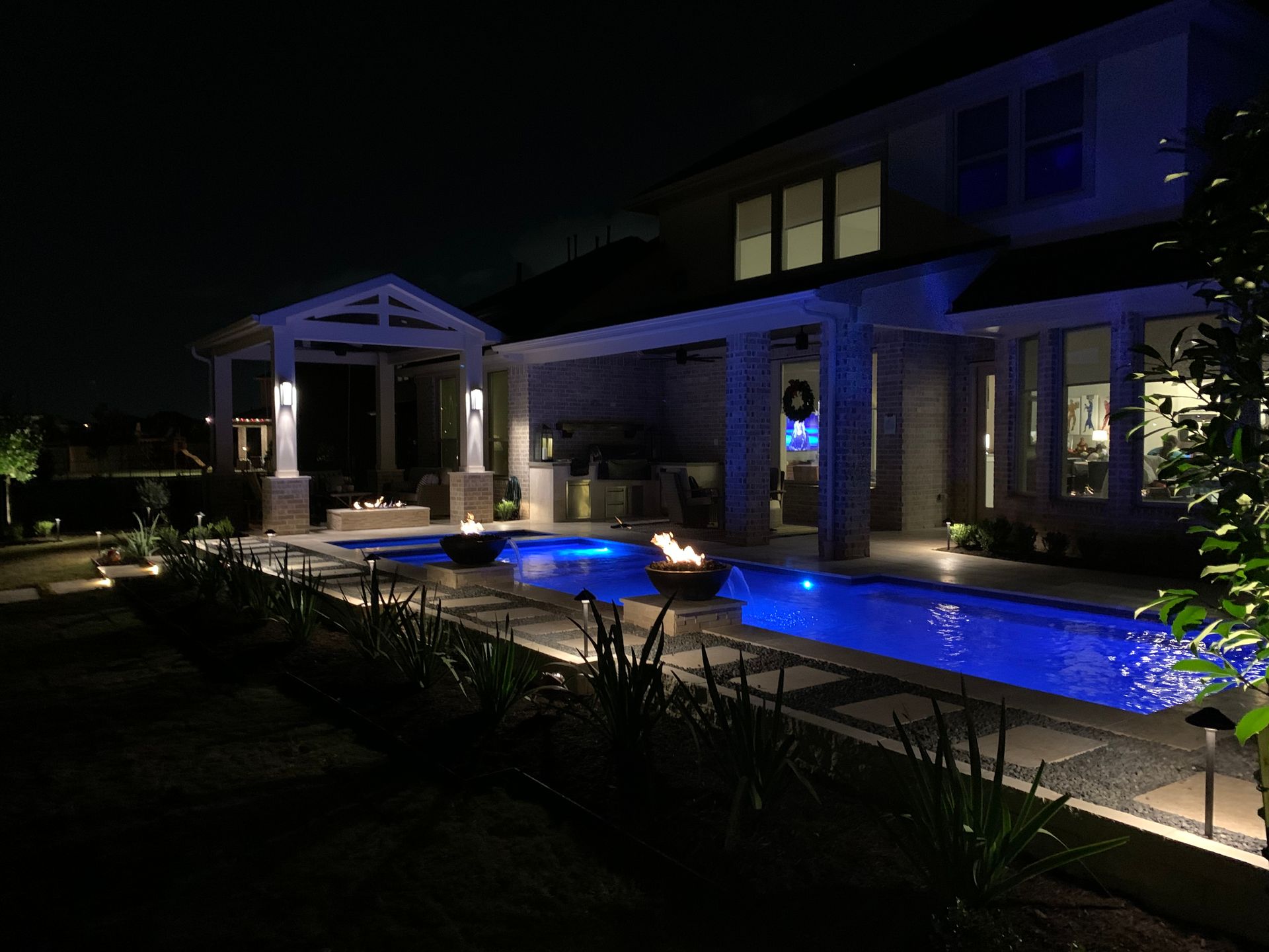 A large swimming pool is lit up at night in front of a house.