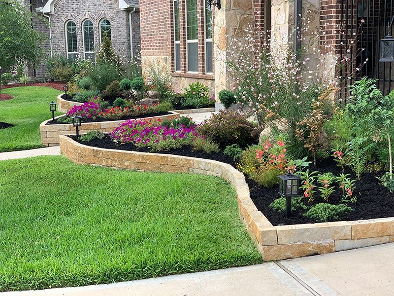 A large brick house with a lush green lawn and flowers in front of it.
