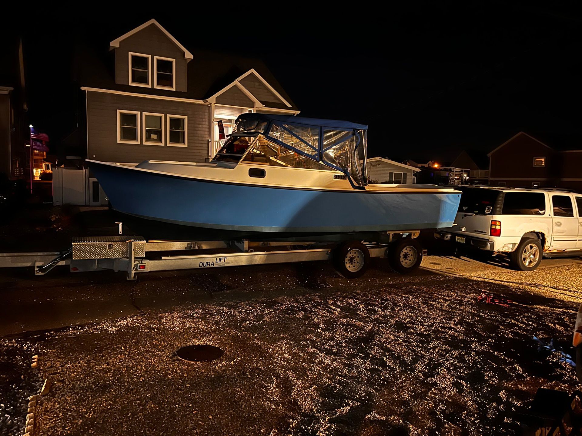 A blue boat is on a trailer in front of a house at night