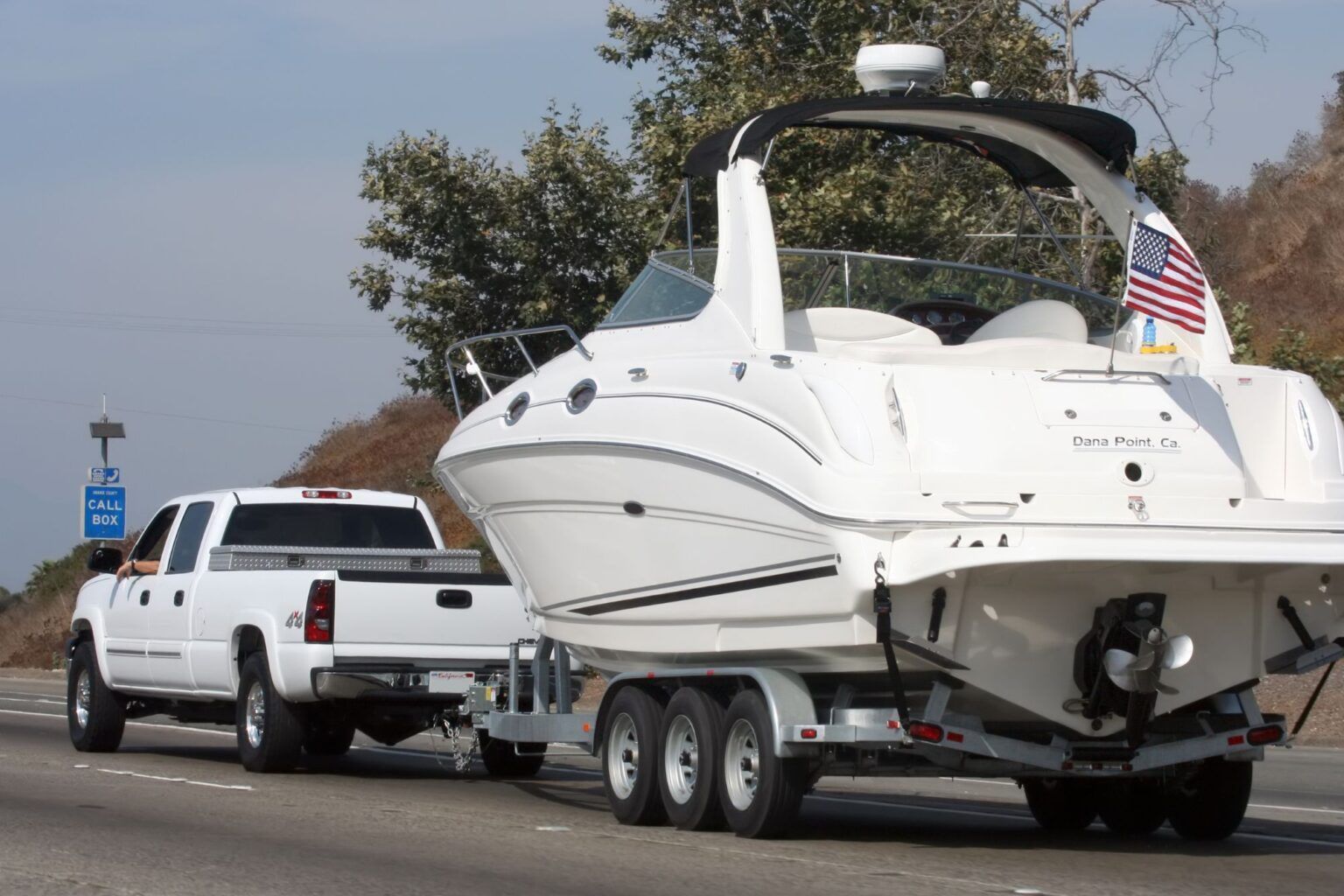 A white truck is towing a boat down a highway.