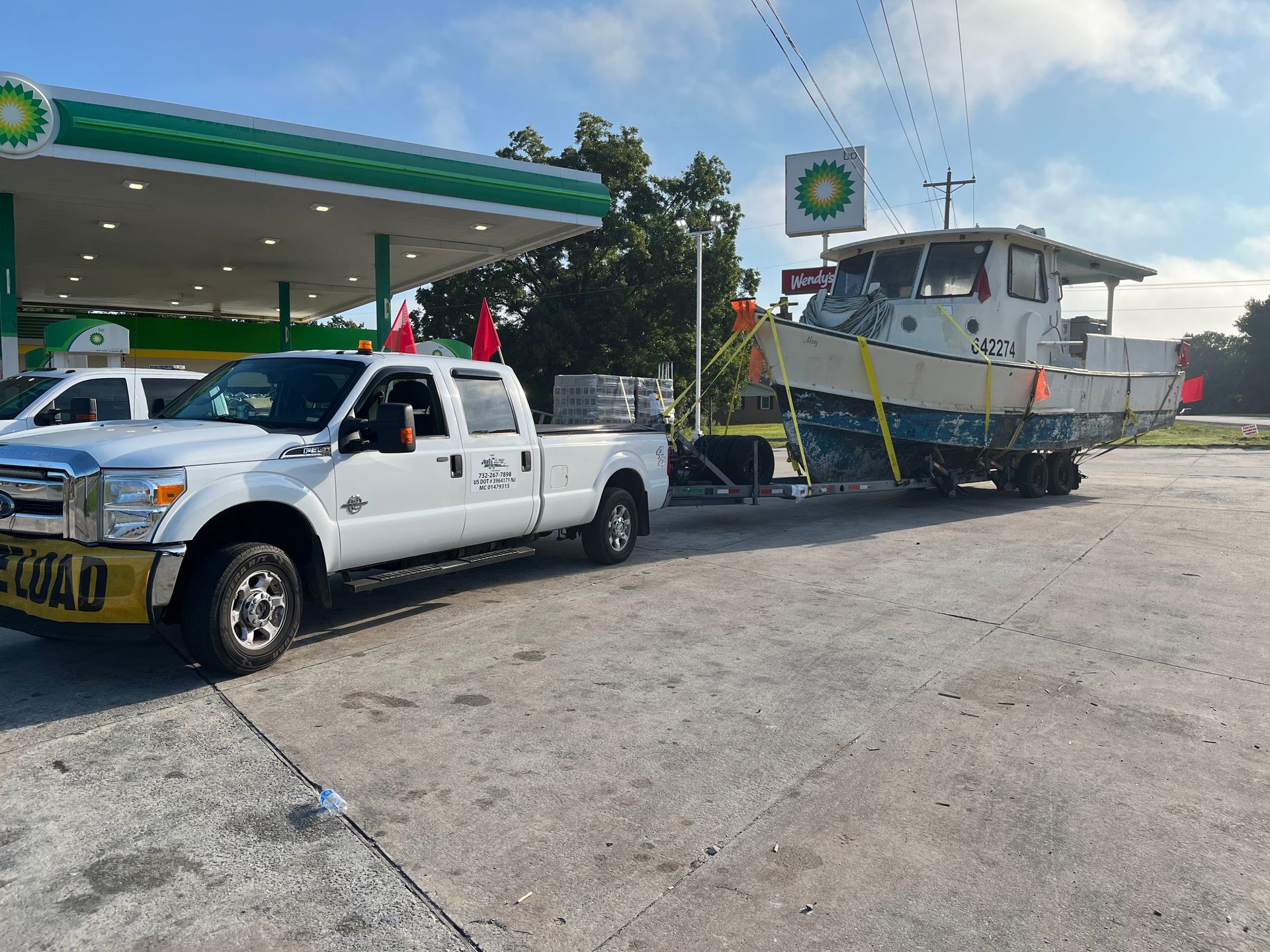 A white truck is towing a boat in front of a bp gas station.