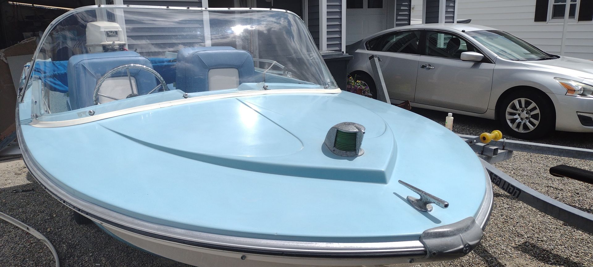 A small blue boat is parked next to a silver car.