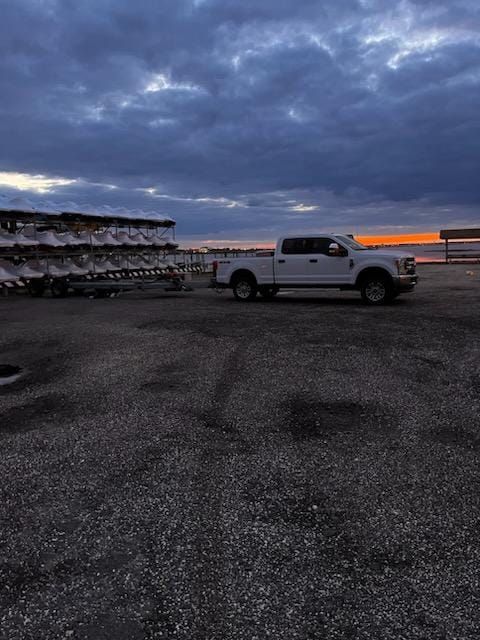 A white truck is parked in a gravel lot next to a trailer.