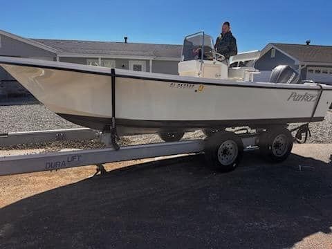 A man is standing next to a white boat on a trailer.
