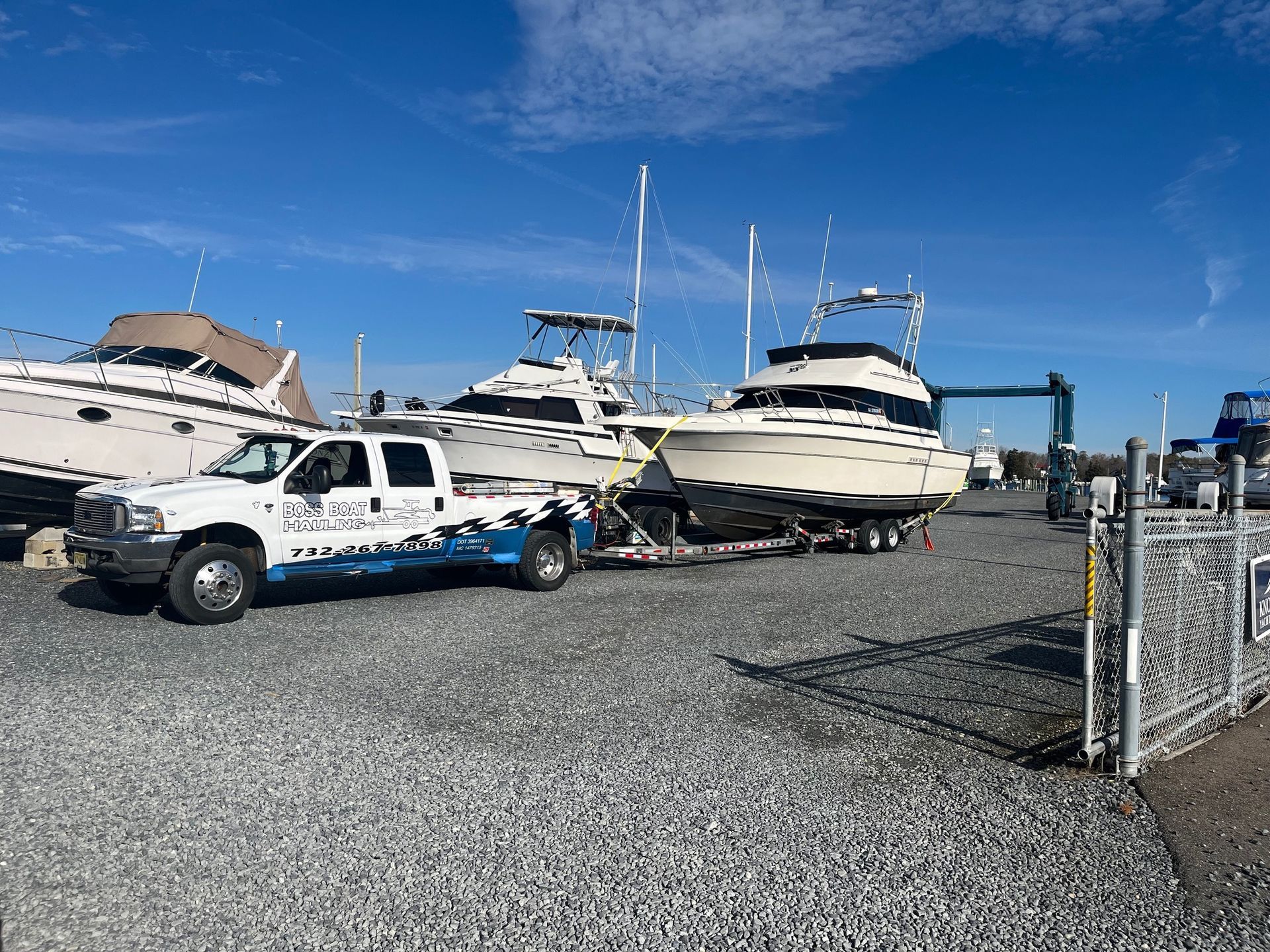 A truck is towing a boat in a gravel lot.