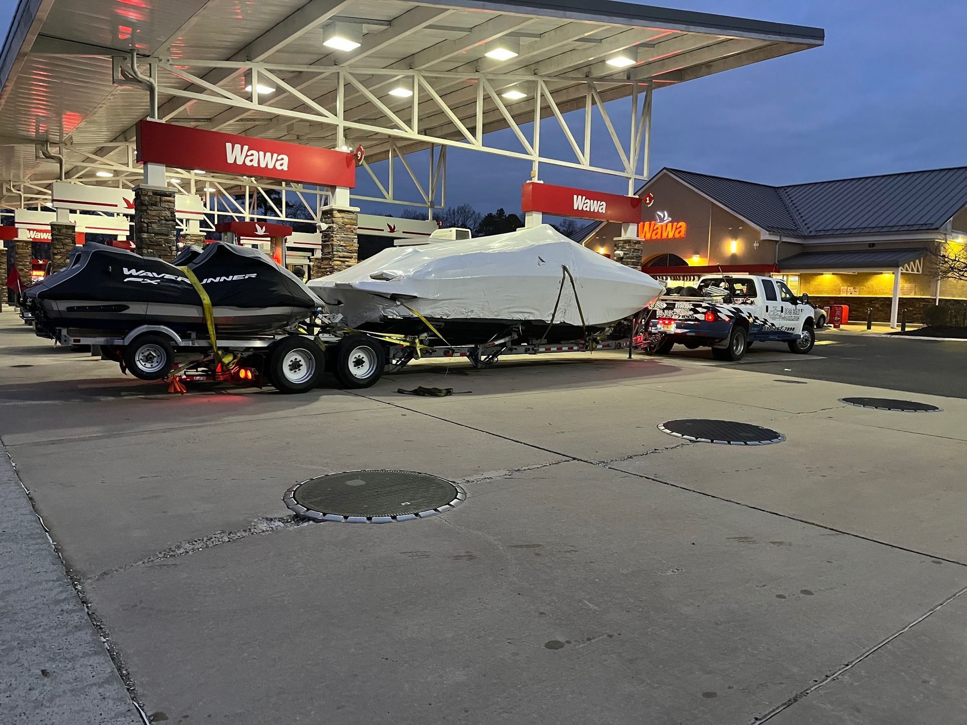 A boat is being towed by a trailer at a gas station.