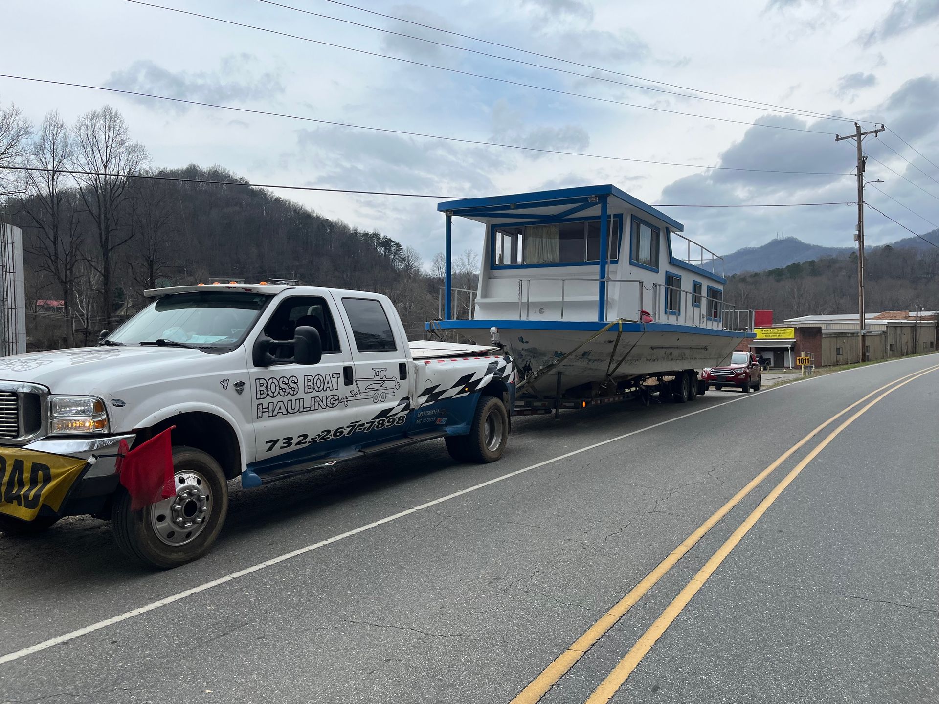 A white truck is towing a boat down a road.