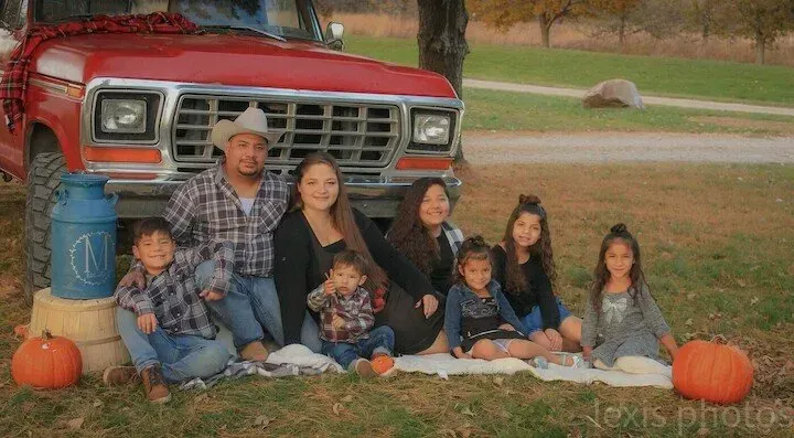 A family is posing for a picture in front of a red truck.