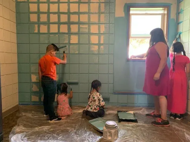 A group of children are painting a wall in a room.