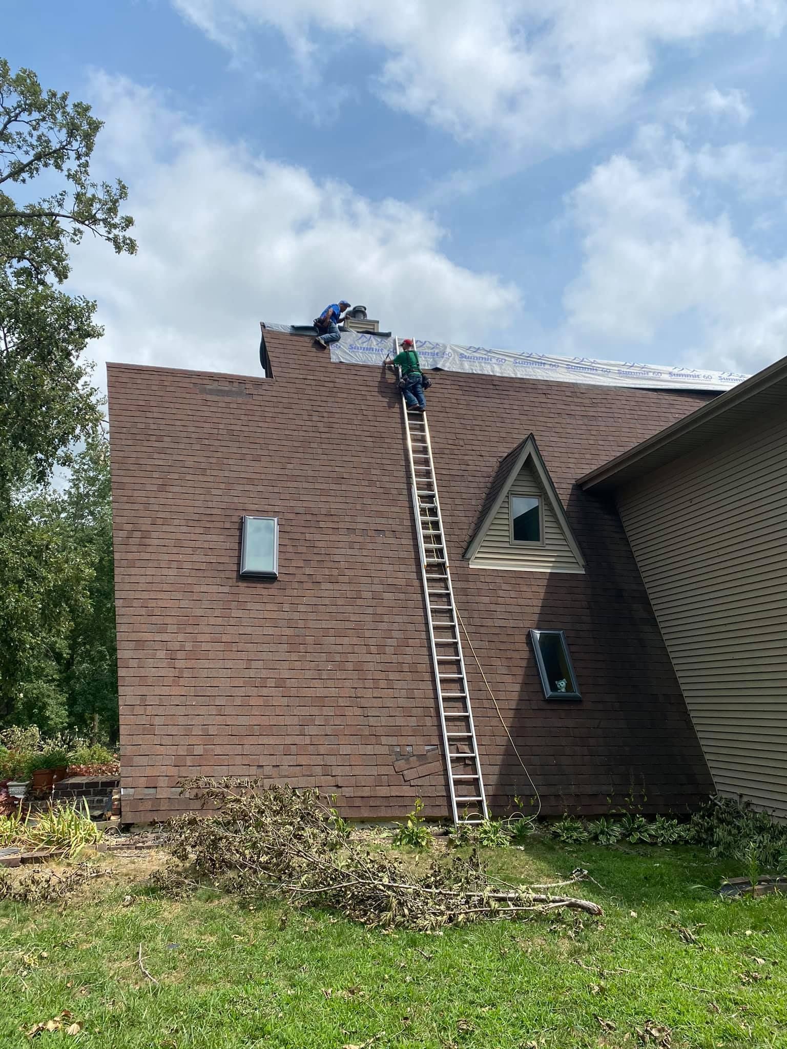 A man on a ladder is working on the roof of a house.